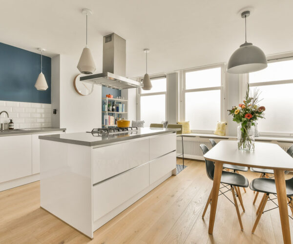 Table with chairs and flowers located near lounge area and kitchen in spacious room of contemporary apartment